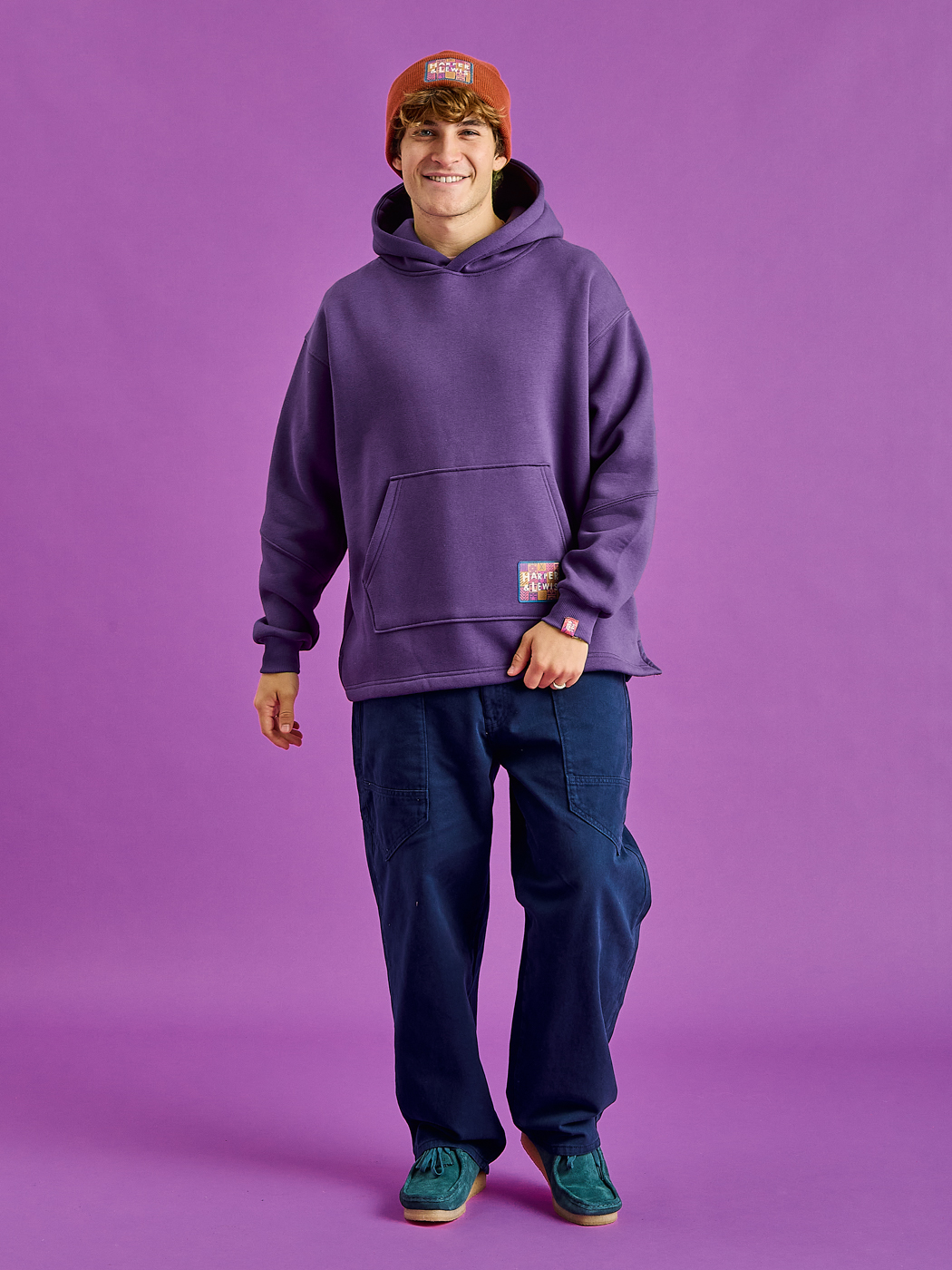 Male Model wears the unisex hoodie in purple, which has subtle detailing all throughout.