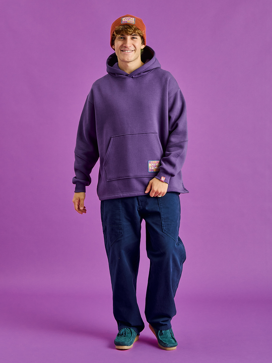 Male Model wears the unisex hoodie in purple, which has subtle detailing all throughout.