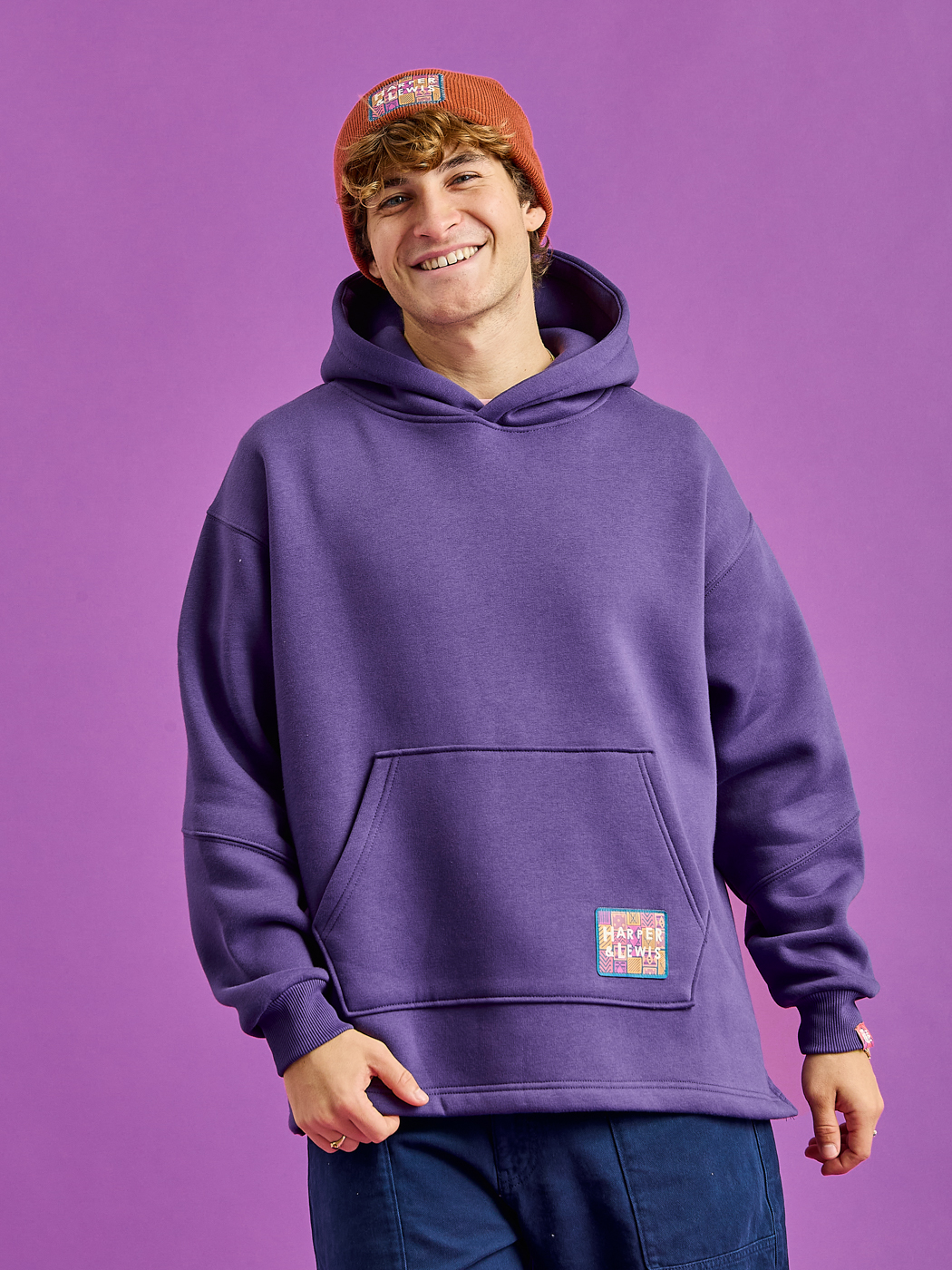 Male Model wears the Indiana Hoodie which features a woven retro inspired branded badge on the front pocket.