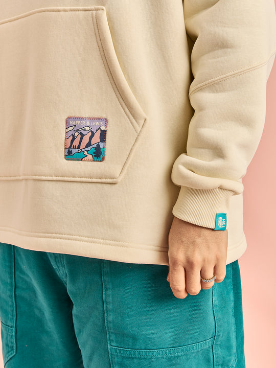 Detail shot: woven branded badge on the front hem of the Willow Hoodie, butter-yellow
