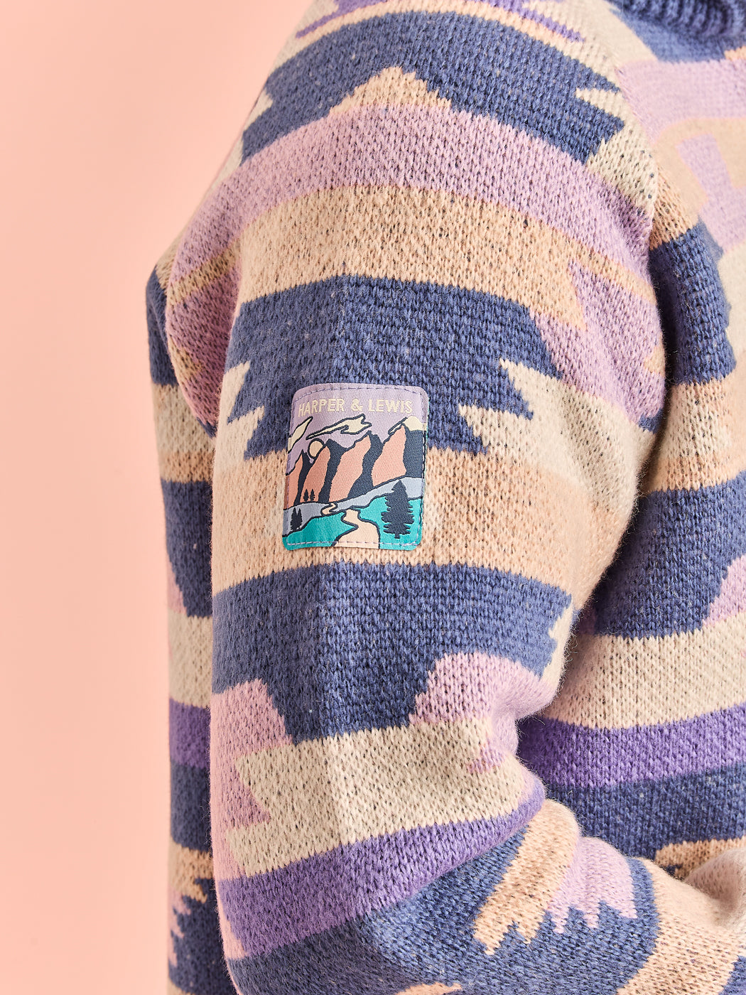Close-up detail shot of the branded woven badge on the sleeve of the knitted jumper.