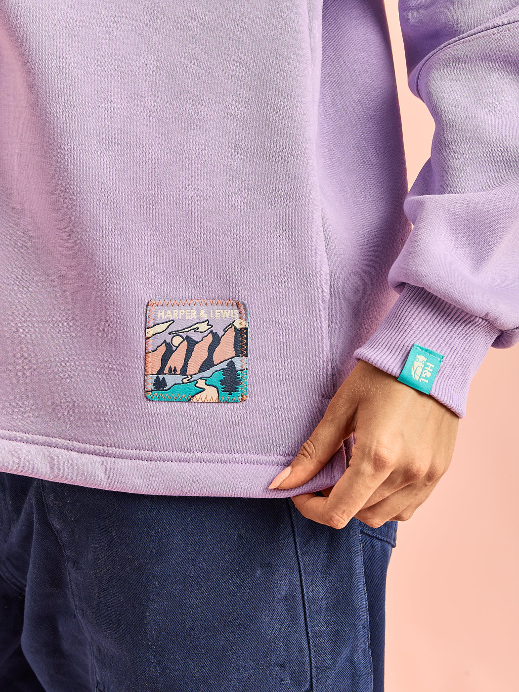 Details of the mountain inspired badge on the hem of the lavender quarter zip 