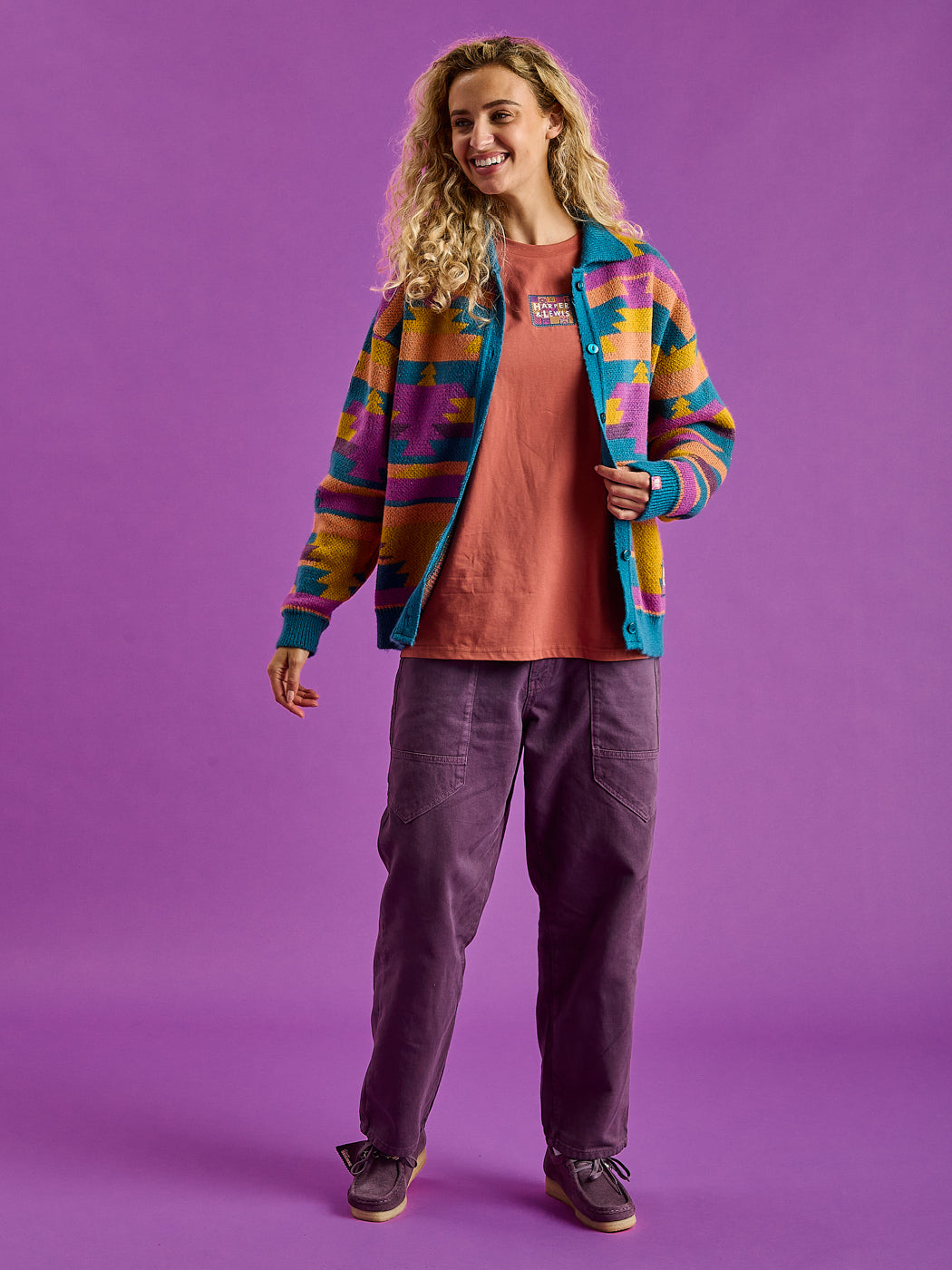 Female Model wears the unisex knitted button up cardigan which features colours of Teal, Dark Rose, Deep Mulberry, Orchid, Deep Peach & Mustard