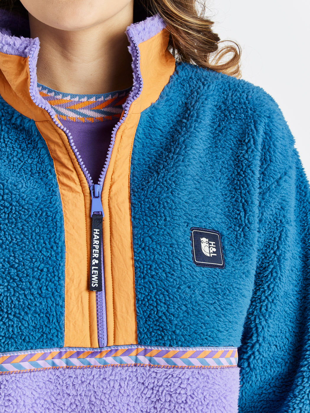 The details of the Logan Sherpa Fleece, branded Zip puller and badge on the chest, also showing the tape detail around the body of the fleece.