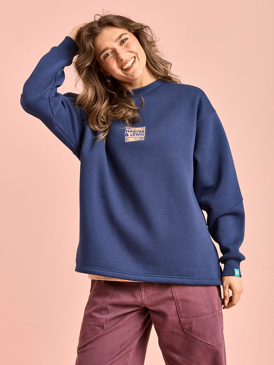 Female model wears the oversized sweater which features a branded front graphic on the chest.