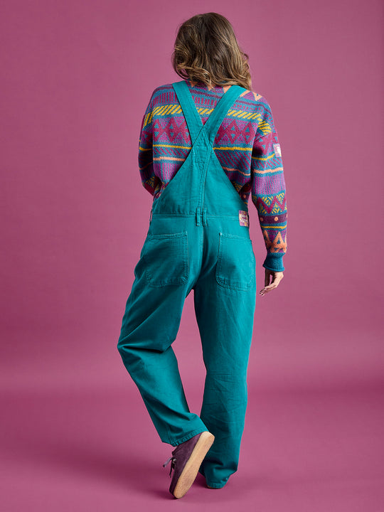 Back shot of the female model wearing the dungarees in a teal green, this shows the back pockets and the belt loops