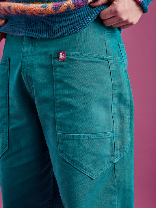 Detailed shot of the front pocket featuring seams and the branded badge on the teal trousers