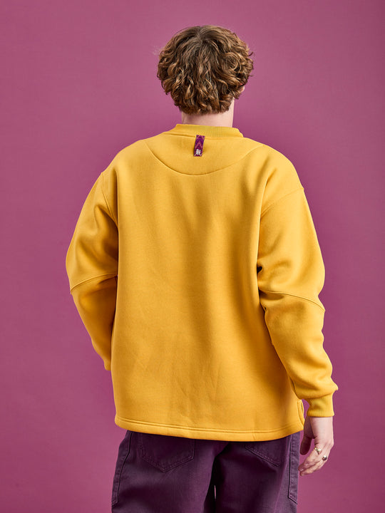Back shot of the male model wearing the Winnie sweater in Mustard yellow, showing the branded woven tab at the back of the neck which can be used as a hanging loop.