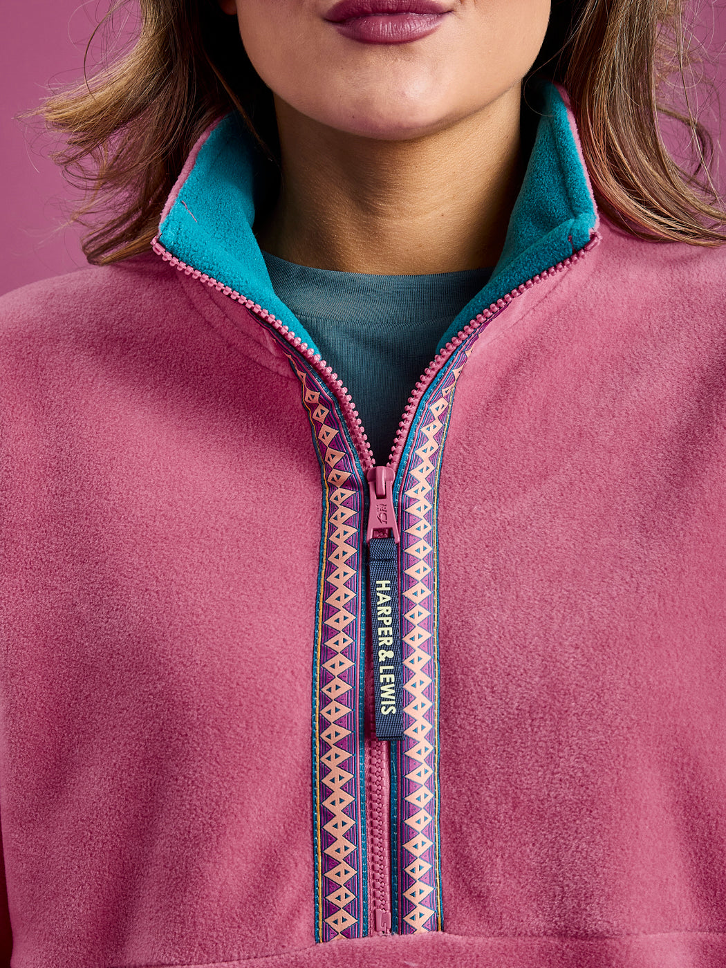 Close up detail of the Fleece Jacket, this shows the branded zip puller, the teal inside collar and the Aztec Wave Pattern woven tape around the zip.