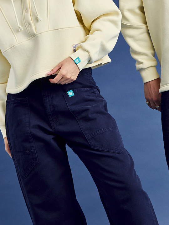 Detail shot of the wrap around pocket featuring a teal branded tab on the pocket of these workwear style trousers