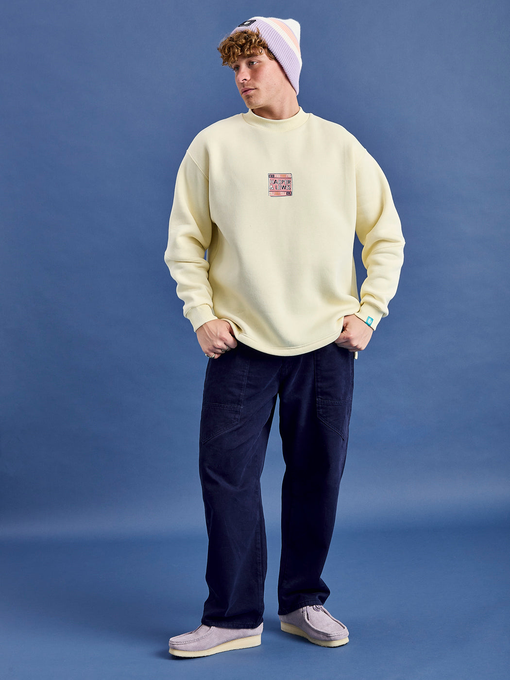 Male Model wears the Cream Sweater styled with the Asani Trousers in Navy.