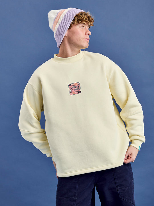 Male Model wears the oversized sweat in a cream colour featuring a print on the front chest.