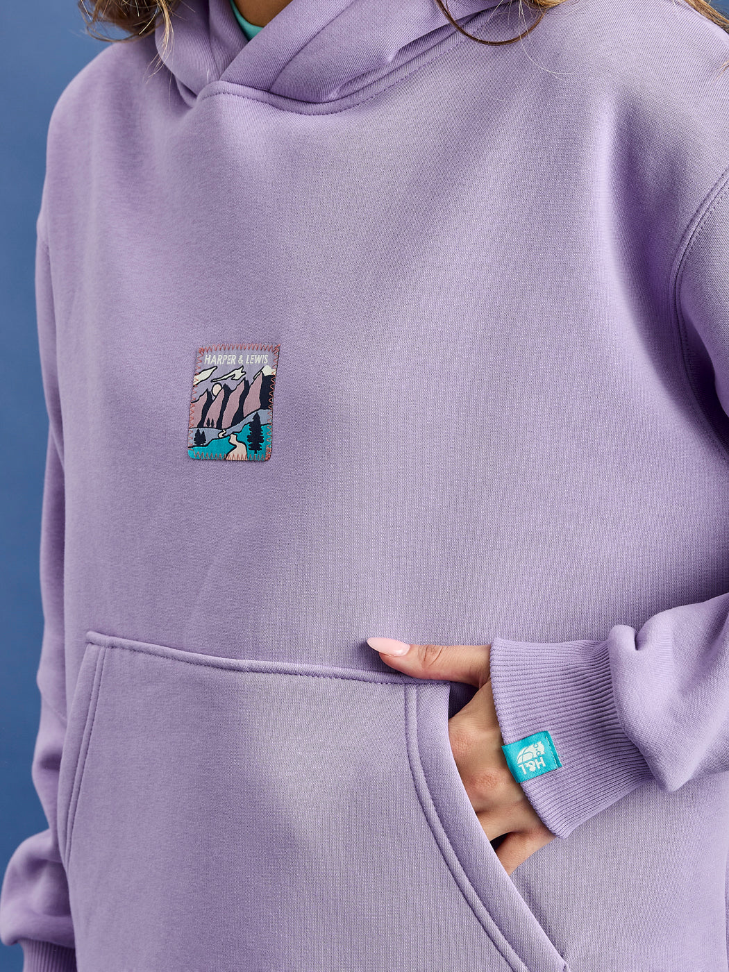 detailed shot of the front badge which has a zigzag stitch attachment and a woven tab in teal on the sleeve.