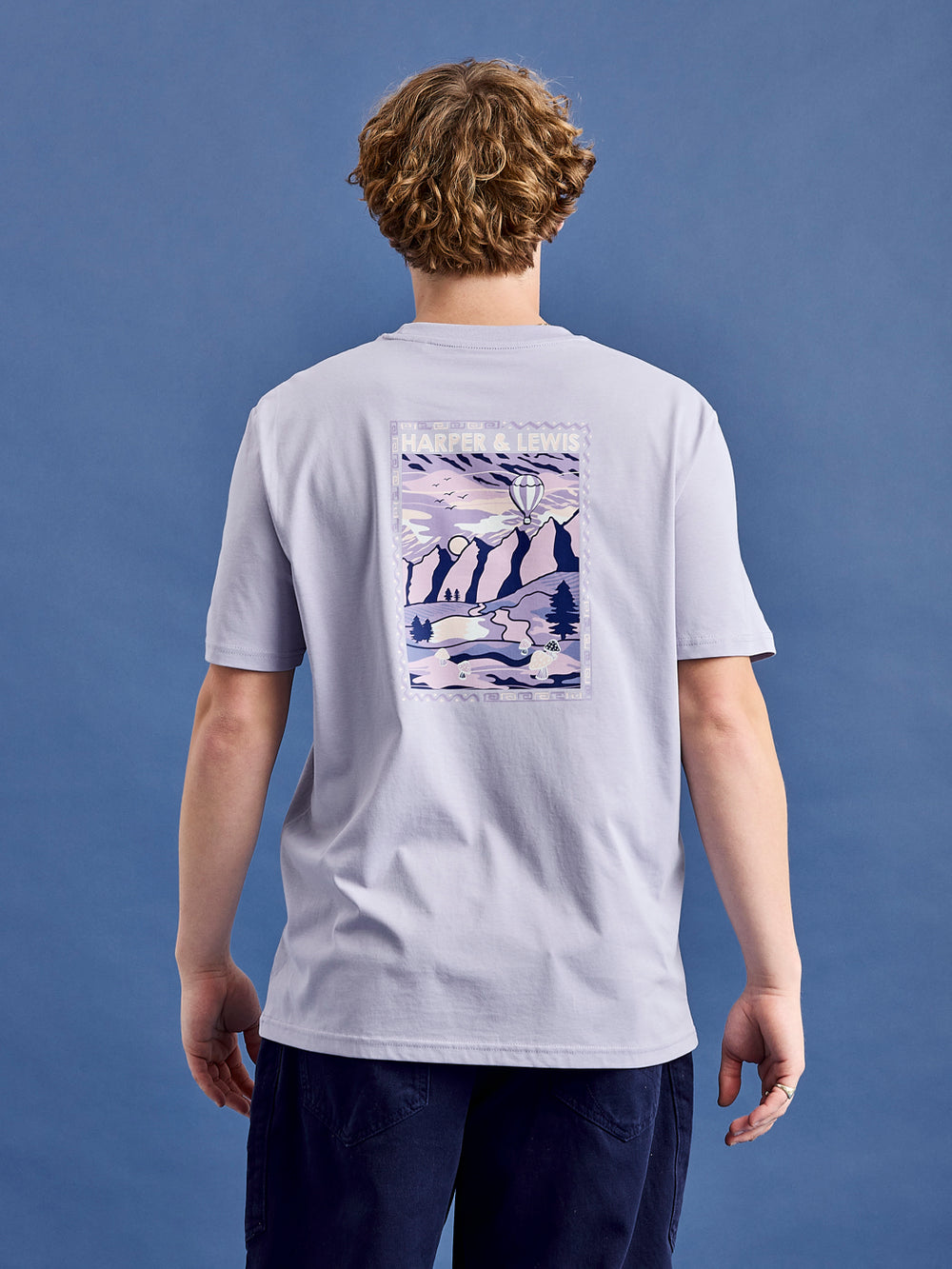 Male Model wears the Atlas t-shirt in Lavender, this has a back print with is inspired by mountain adventure