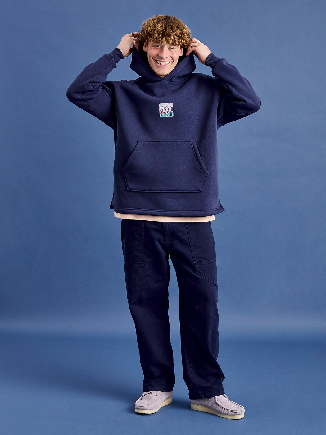 Male Model wears the Ellerie Hoodie in navy which is made from a robust blend of 65% Cotton and 35% Polyester