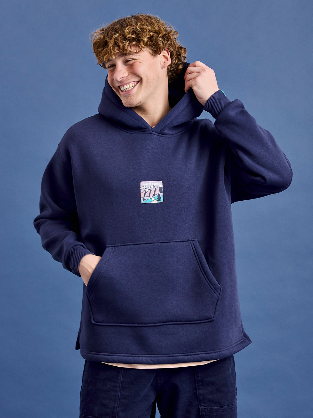 Male Model wears the Ellerie Hoodie in Navy which features a released hem for maximum comfort.