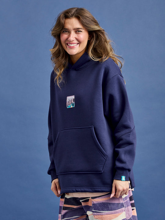 Female Model wears the Ellerie hooded sweater in navy, which features a kangaroo front pocket and an oversized hood.