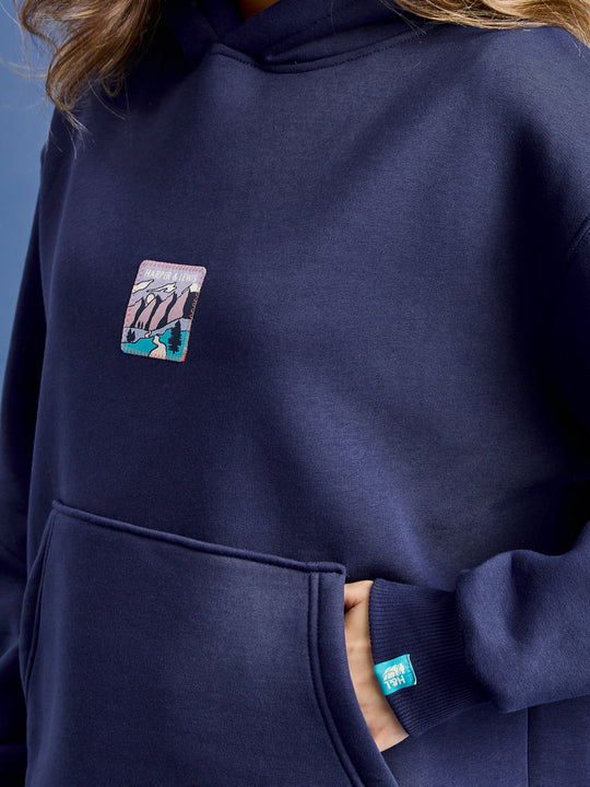 Detail shot of the mountain adventure inspired front badge and the teal branded tab on the cuff.