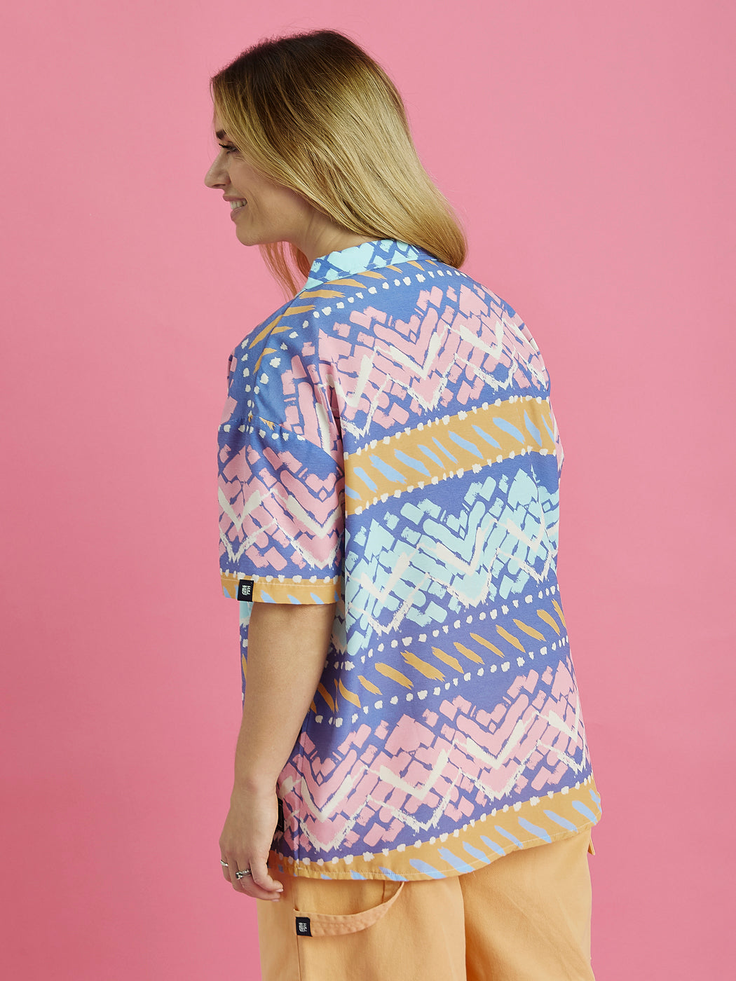 Female model facing away from the camera showing the back of the shirt and the sleeve tab. This shirt is your ideal choice for standout, vibrant style.