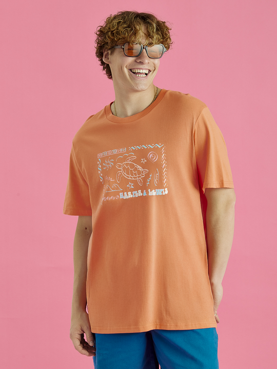 Male Model wearing the relaxed fit Surya tee in Apricot, this tee features a big front chest logo design.