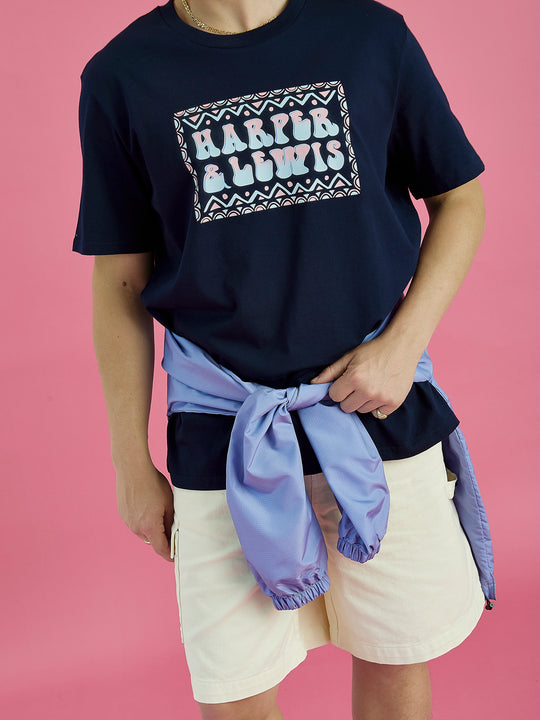 Male models wears the Taran tee in navy, this is styled with the Ottis shorts in cream with the Rene 1/4 Zip Hooded Jacket tide around the waist.