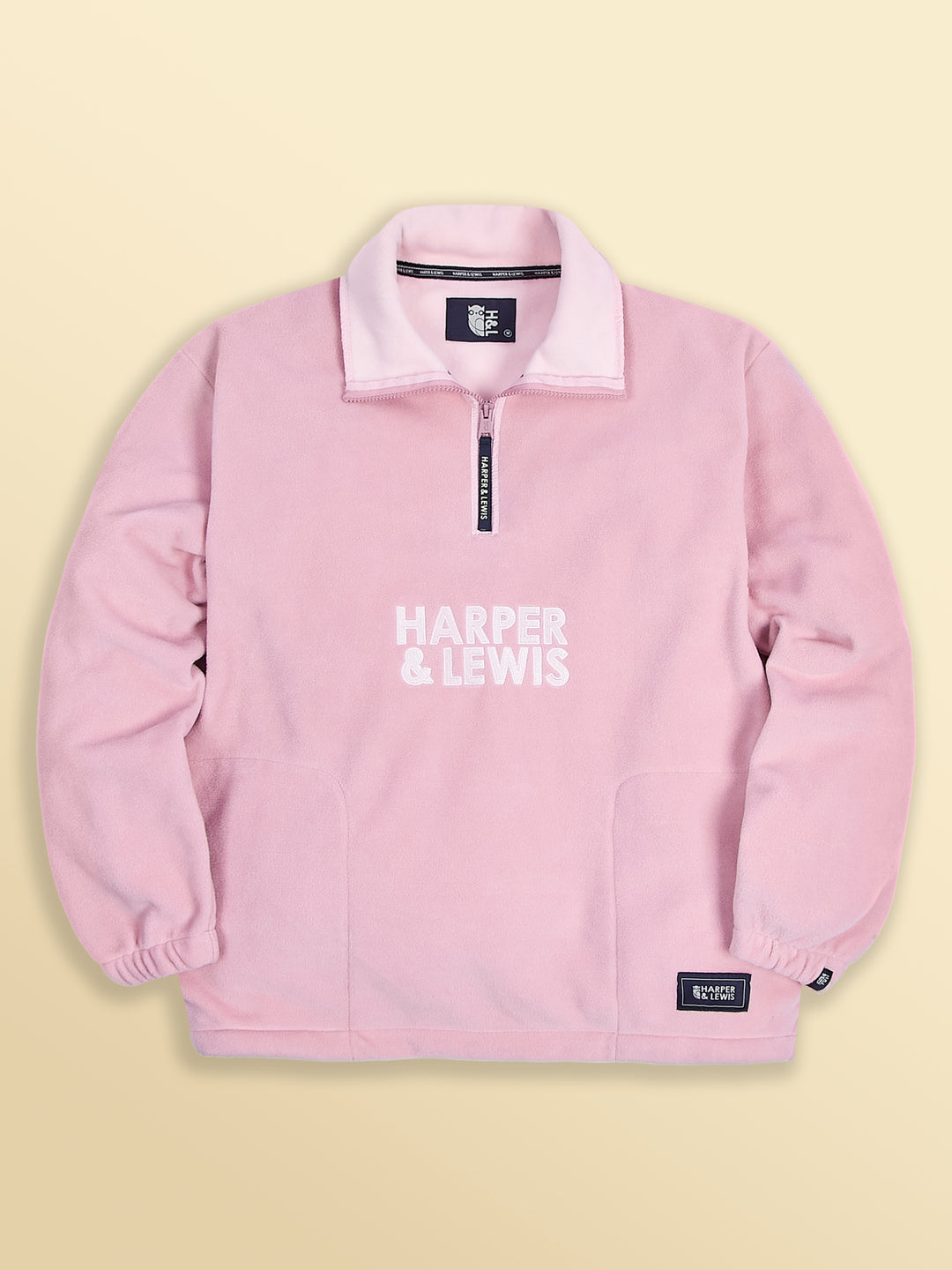 Flatlay of the Elsa unisex dusty pink fleece ,showing all of the details including the branded patches and embroidery.